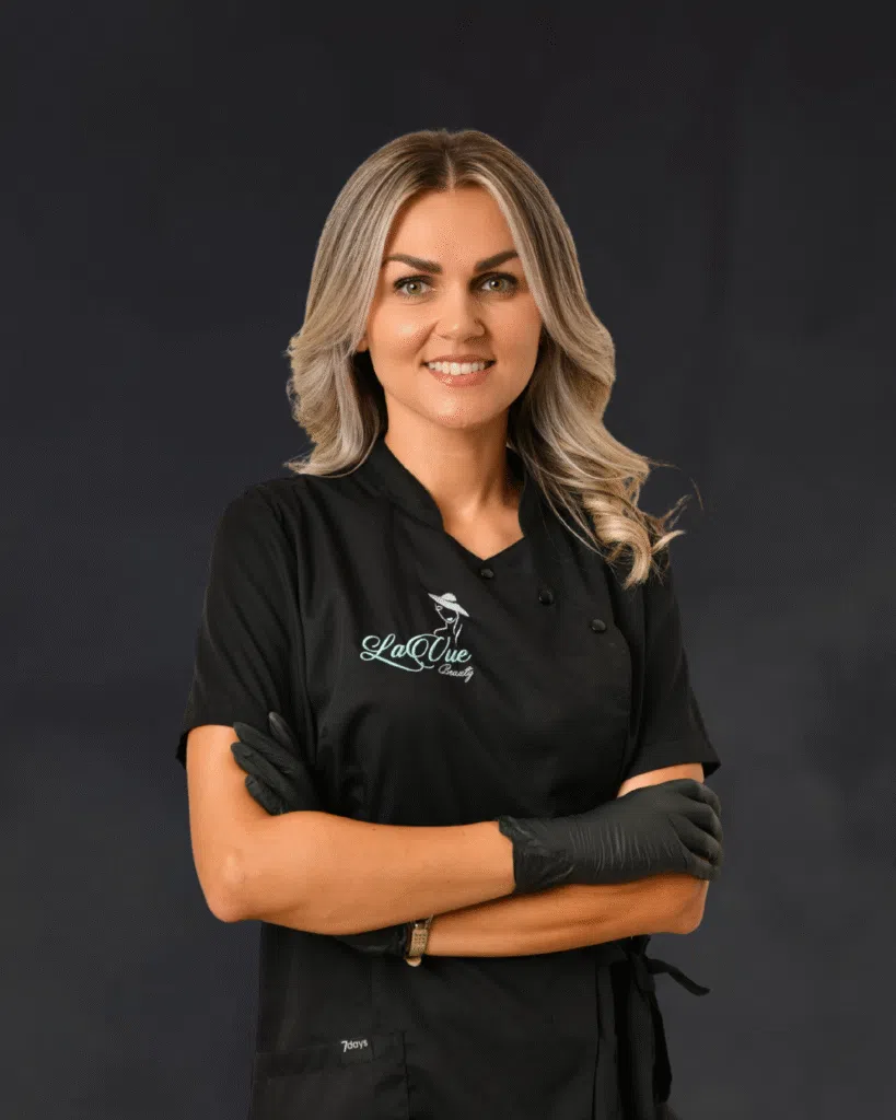 Danijela Atanasovska Gründerin und Artist von LaVuebeauty auf schwarzem nebeligem Hintergrund. Lächelnd und mit eingeschlagenen armen. Mittig ausgerichtet.