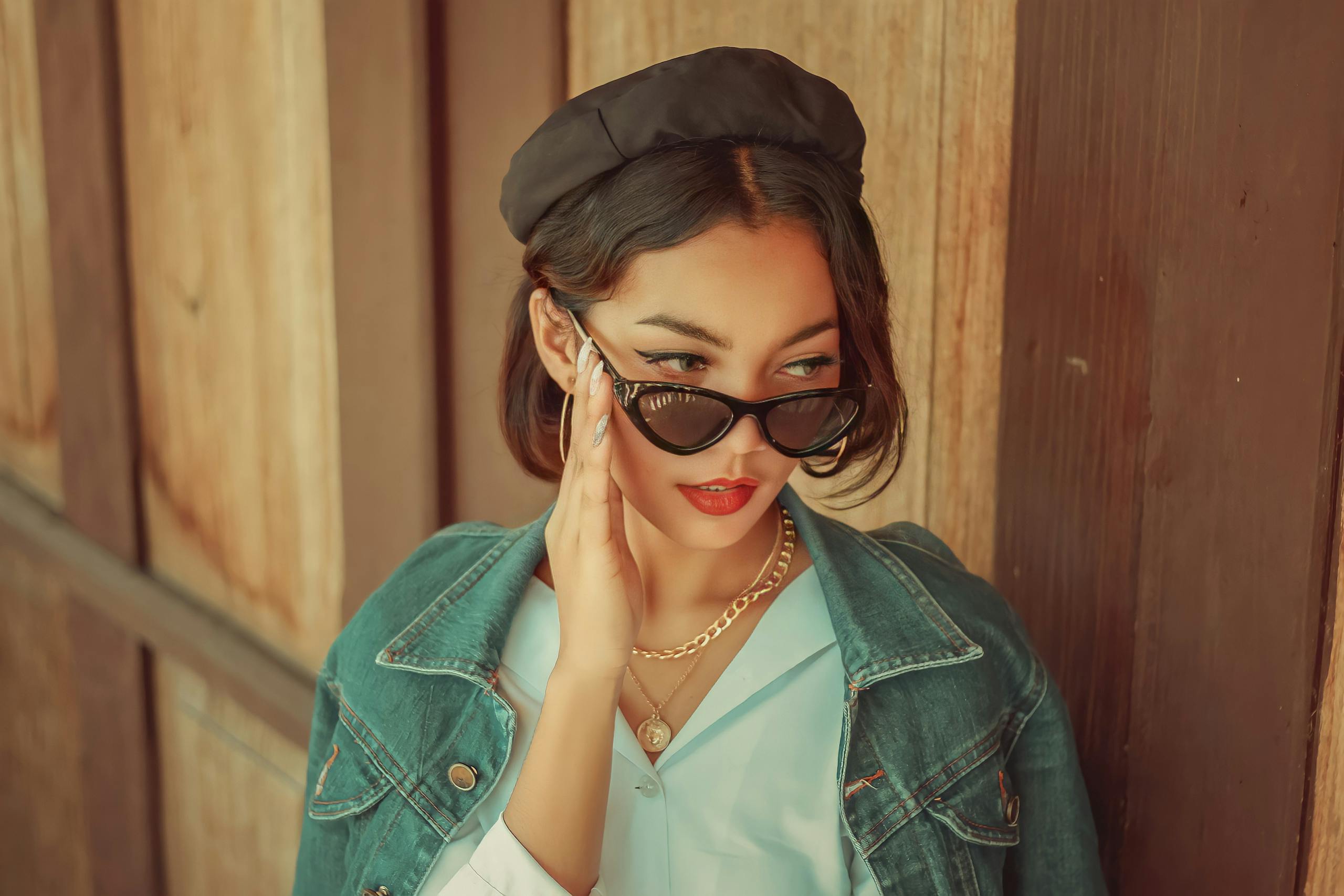 Fashionable woman in denim jacket and sunglasses poses confidently outdoors.