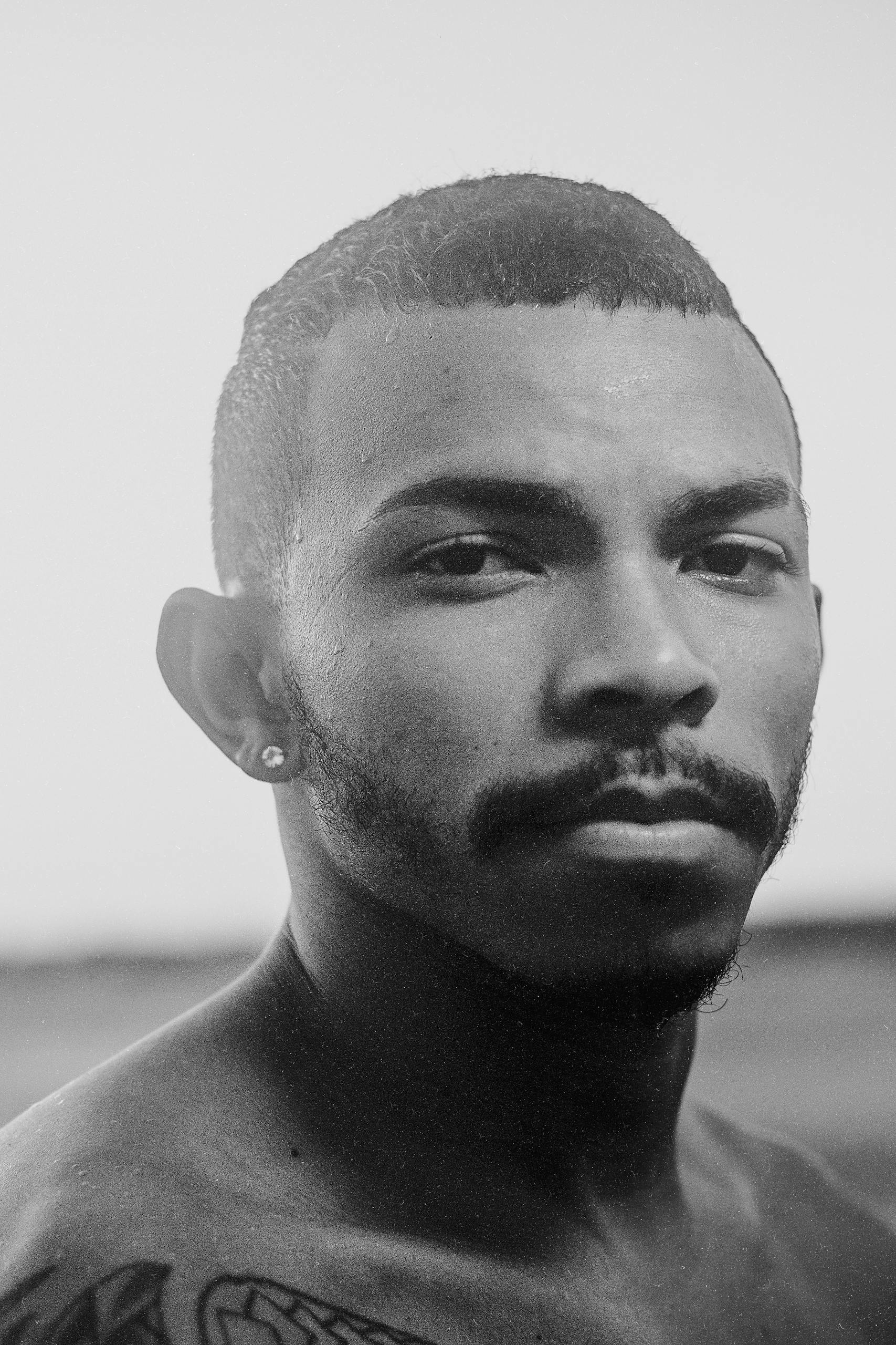 Black and white close-up portrait of a shirtless man with a mustache, exuding confidence.