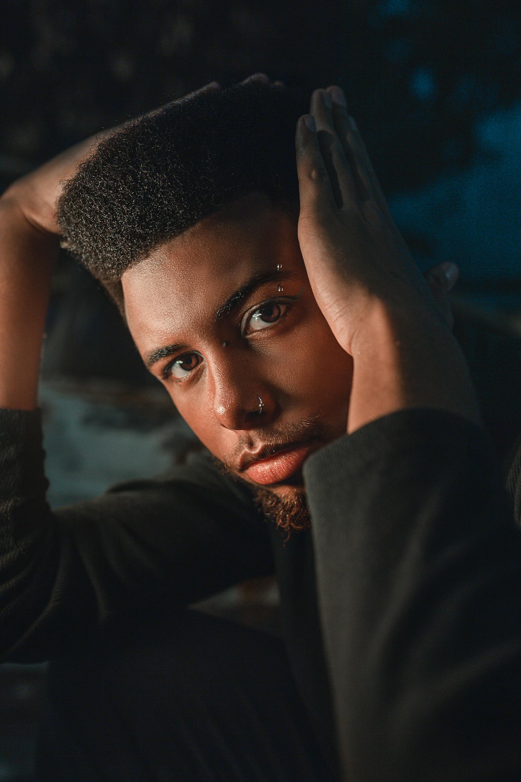 Close-up portrait of a young black man with piercings, looking thoughtfully at the camera.