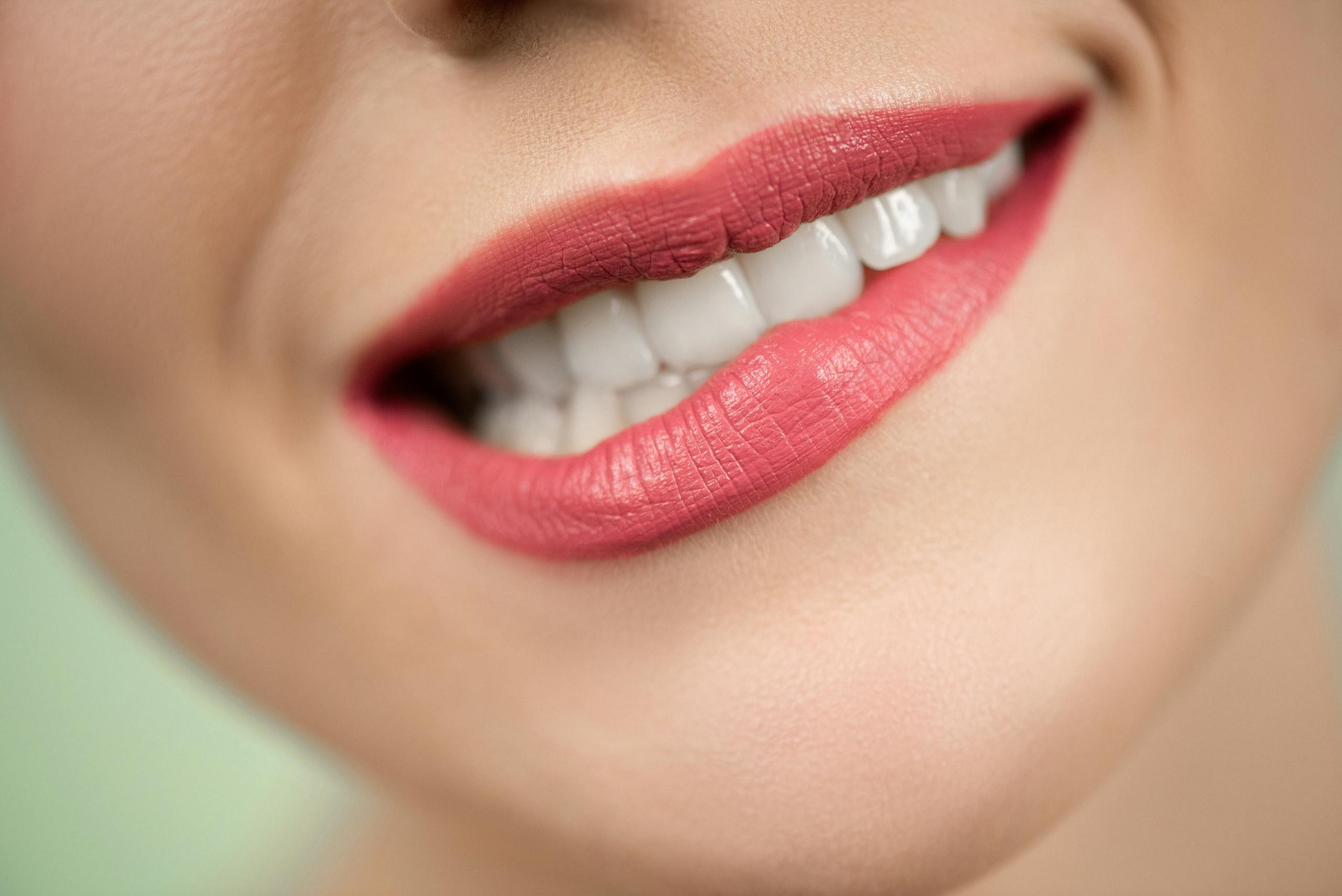 Close-up shot of woman's mouth wearing red lipstick, highlighting bright teeth and smooth skin.