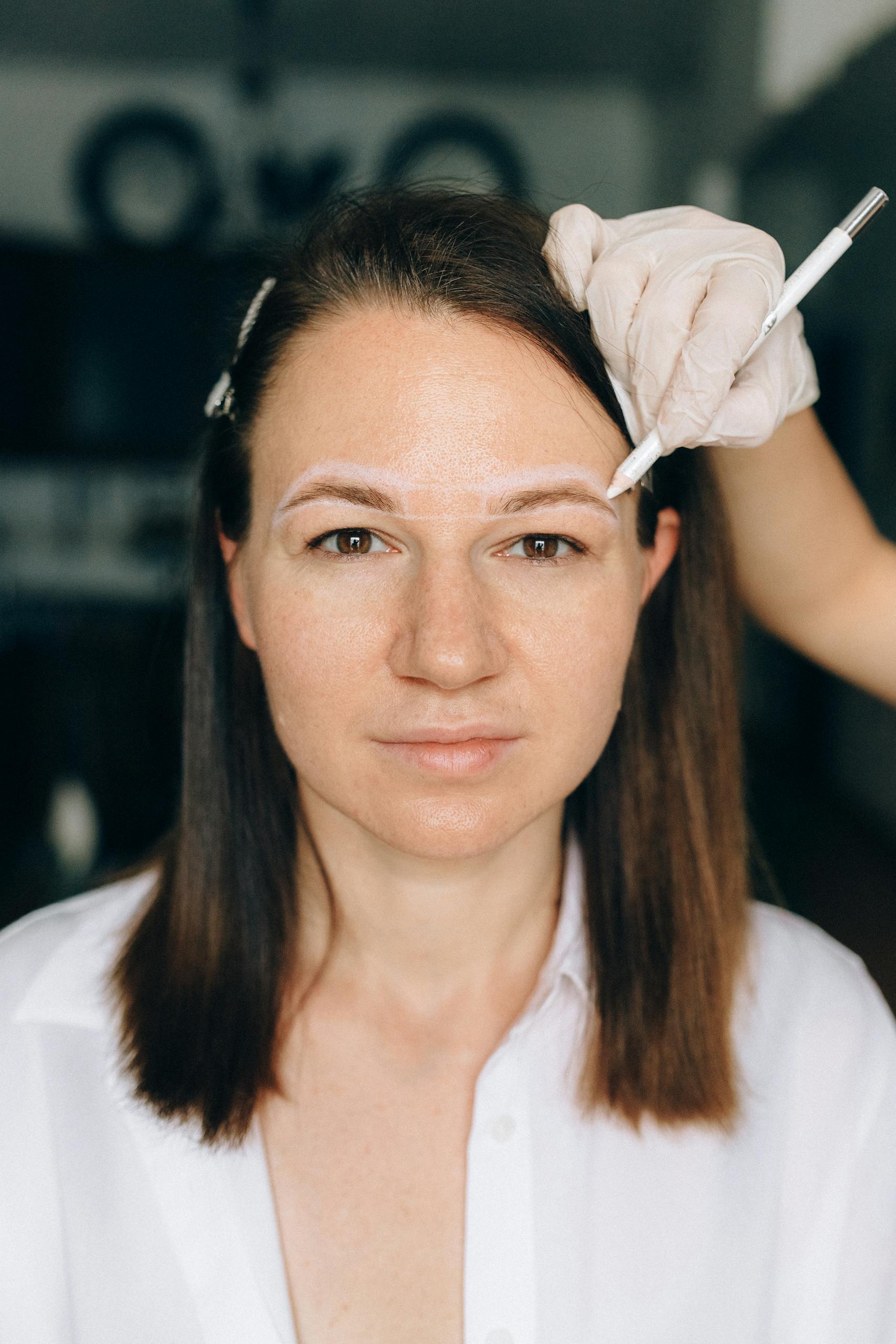 A middle-aged woman receives a cosmetic eyebrow procedure by a professional beautician.