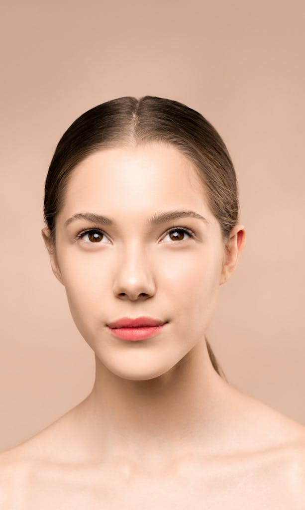 Studio portrait of a woman with clear skin and soft expression on a neutral background.